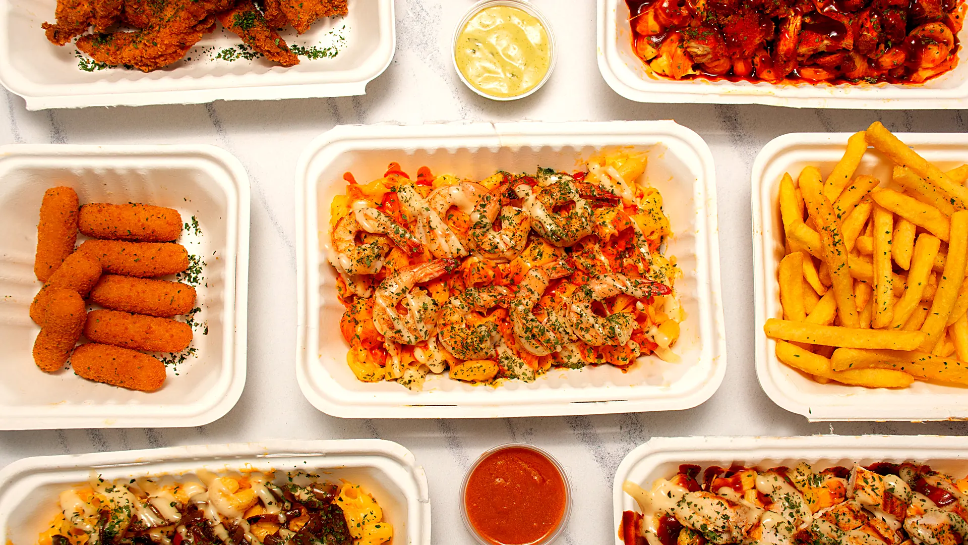 A spread of Mac'd Up bowls, tenders, chips, mozzarella sticks and dips